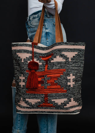 Faded Black, Tan & Red Aztec Tote - Holt x Palm -  Go bold and bohemian with our Faded Black, Tan & Red Aztec Tote! This extra large tote is perfect for carrying all your essentials in style. Embrace your free-spirited side with the timeless Aztec design. It's a tote, it's a statement piece - it's everything you need. Aztec-chic never looked so good! Description: Faded black, tan, red & rust Aztec tote w/ Red pom tassel detail 17" x 6.5" x 14.5" 100% Cotton Min.