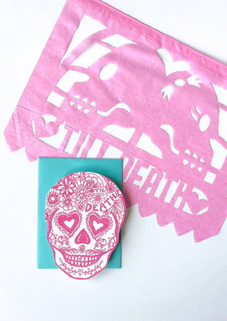 Til Death Sugar Skull Card - Holt x Palm -  til death! A card based on the Sugar Skull. • blank inside and measures 4.25”x5.5” folded • shaped folded card is letterpress printed in rhodamine ink on 110# cotton paper • die cut • accompanied by an A2 blue raspberry envelope and packaged in a clear sleeve