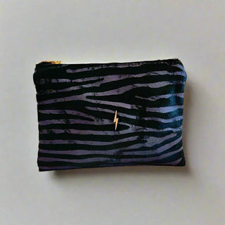 Emerald Zebra Bolt Pouch - Holt x Palm -  This Bolt Pouch is made from high-quality Italian leather with a hair-on pewter zebra effect. It features a stylish gold bolt accent. It is lined with plush rust velvet and has a heavy-duty Italian zipper for added durability. The pouch also includes a small interior pocket for extra organization. Approximate dimensions: 7.75" W x 6" H. Handcrafted in the USA