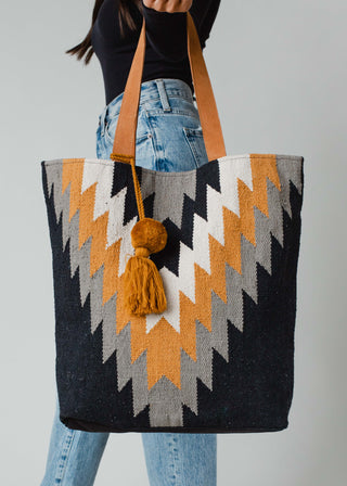 Must Have! Black, Gray, Mustard & Cream Aztec Tote - Holt x Palm -  Stay on trend with our Must Have! Black, Gray, Mustard & Cream Aztec Tote. This bohemian-inspired bag features a cool and unique aztec design, making it the perfect statement piece for any outfit. Get ready to stand out in style! Black, gray, mustard & cream Aztec tote Mustard Pom tassel detail 17" x 6.5" x 14.5" 100% Cotton Min. Qty. 2