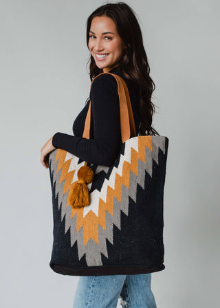 Must Have! Black, Gray, Mustard & Cream Aztec Tote - Holt x Palm -  Stay on trend with our Must Have! Black, Gray, Mustard & Cream Aztec Tote. This bohemian-inspired bag features a cool and unique aztec design, making it the perfect statement piece for any outfit. Get ready to stand out in style! Black, gray, mustard & cream Aztec tote Mustard Pom tassel detail 17" x 6.5" x 14.5" 100% Cotton Min. Qty. 2