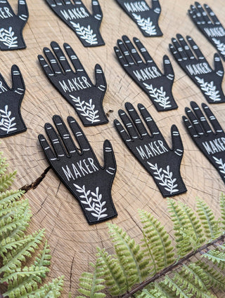 Hand Maker Patch - Holt x Palm -  A hand-shaped patch with the word "maker" on the palm along with ferns adorning the wrist. Based on a linocut print by ilikesara / Sara Schalliol-Hodge. -black & white -2.56" x 3.9" -iron-on backing instructions for ironing: Place the patch on your garment and cover the patch with a piece of fabric. Iron on high heat for 30-45 seconds. Turn the garment inside-out and iron on reverse side of the patch for 30-45 seconds.