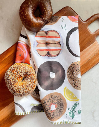 Bagel Tea Towel - Holt x Palm -  Our vibrant tea towels are just the thing to add a touch of colorful flair to your kitchen! Woven from 100% absorbent cotton and printed with our charming, hand-painted designs, each towel is embellished with contrasting embroidery along the seaming. This Tea Towel features whimsical hand-painted donut illustrations in every variety, color, and shape. • 21″ X 28″ • HANGING LOOP • EMBROIDERED TRIM • PACKAGED WITH HANGING CARD • MATCHING OVEN MITT + POT HOLDER SET