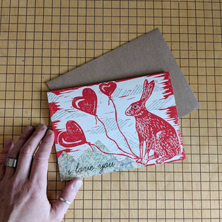 Greeting card | i love you bunny - Holt x Palm -  i love you bunny Show some bunny you love them with this card. Reproduced from an original mixed-media block print by ilikesara / Sara Schalliol-Hodge, which features collaged map mountains, text clouds, and linocut printing. Card measures 4.25" x 5.5" when folded. Printed on 100 lb cream cover paper. Kraft envelope included. Blank interior. Packaged in a clear cellophane sleeve. Designed and printed in Denver, Colorado.