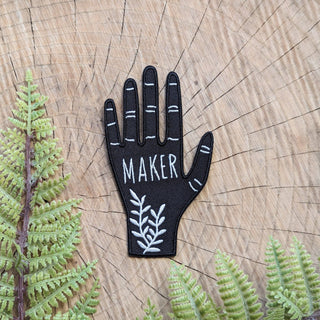 Hand Maker Patch - Holt x Palm -  A hand-shaped patch with the word "maker" on the palm along with ferns adorning the wrist. Based on a linocut print by ilikesara / Sara Schalliol-Hodge. -black & white -2.56" x 3.9" -iron-on backing instructions for ironing: Place the patch on your garment and cover the patch with a piece of fabric. Iron on high heat for 30-45 seconds. Turn the garment inside-out and iron on reverse side of the patch for 30-45 seconds.