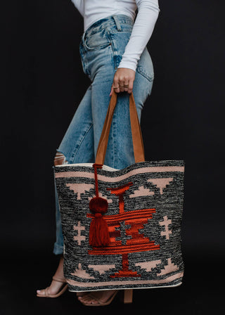 Faded Black, Tan & Red Aztec Tote - Holt x Palm -  Go bold and bohemian with our Faded Black, Tan & Red Aztec Tote! This extra large tote is perfect for carrying all your essentials in style. Embrace your free-spirited side with the timeless Aztec design. It's a tote, it's a statement piece - it's everything you need. Aztec-chic never looked so good! Description: Faded black, tan, red & rust Aztec tote w/ Red pom tassel detail 17" x 6.5" x 14.5" 100% Cotton Min.