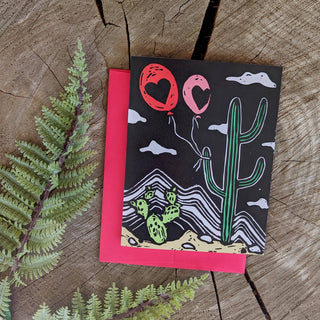 Greeting card | cacti balloon - Holt x Palm -  Even things that are a little prickly can find ways to love. Reproduced from an original linocut block print by ilikesara / Sara Schalliol-Hodge. -measures 4.5" x 5.5" when folded -printed on 100 lb white cover paper -includes red envelope -blank interior -shipped in a clear cellophane sleeve inside a rigid cardboard mailer -designed and printed in Denver, Colorado